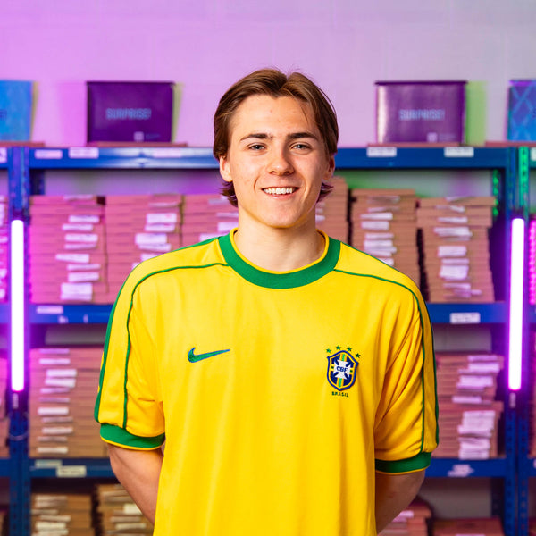 Louis smiles at the camera, wearing a yellow Brazil 1998 home shirt